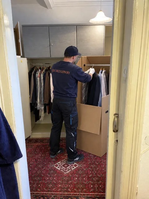 Mitarbeiter vom Umzugsprofi hängt Kleidung aus dem Schrank in eine Kleiderbox