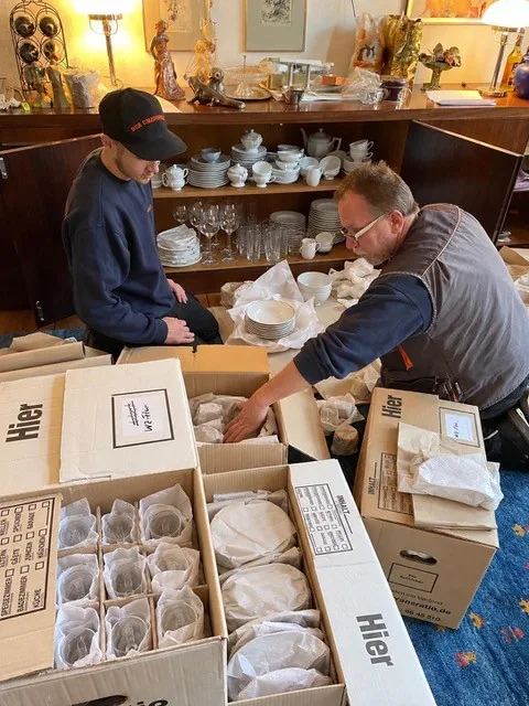 Zwei Mitarbeiter vom Umzugsprofi verpacken Porzellan und Gläser sorgfältig in Umzugskartons